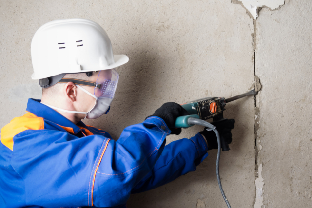 Concrete wall repair being done by worker with a power tool.